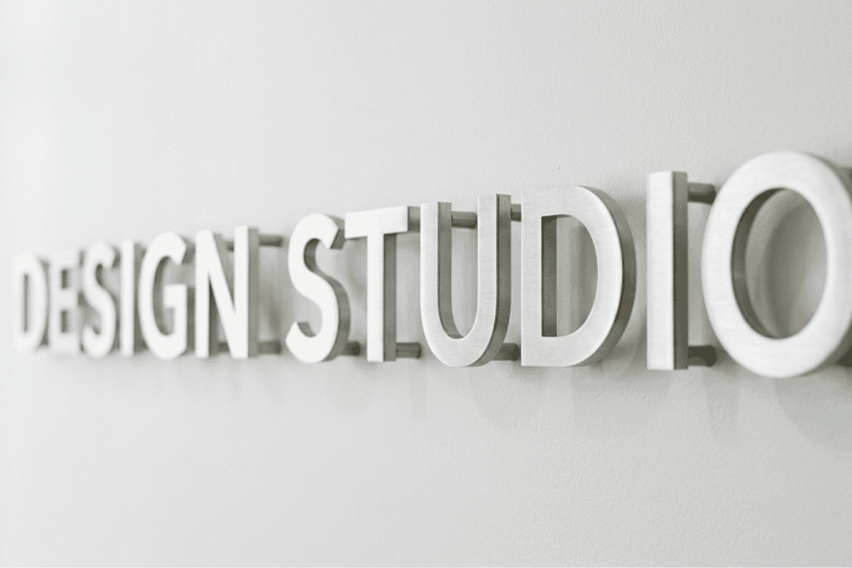Three-dimensional metal letters spell DESIGN STUDIO mounted on a light gray wall.