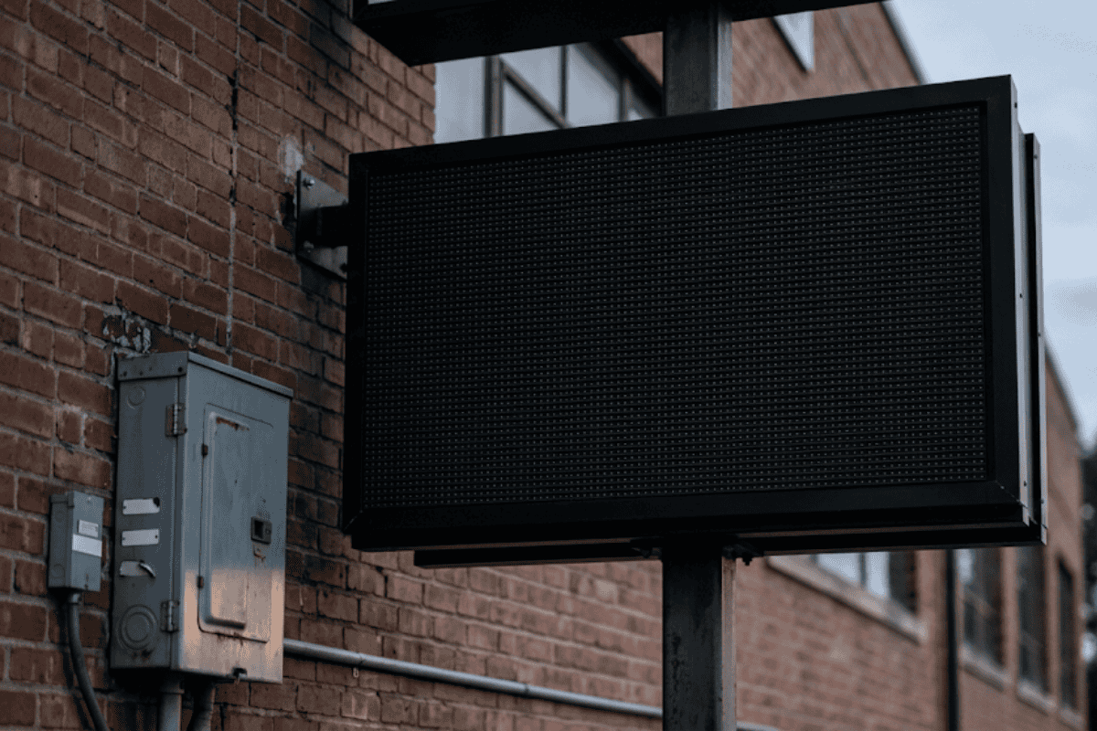 Large empty electronic LED sign mounted on a metal frame in front of a brick building.