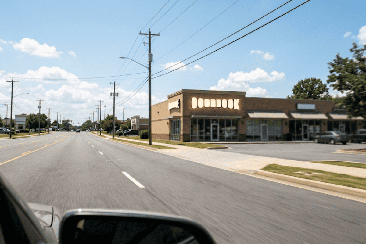 Sunny suburban street with a brick storefront row on the right and a bright blue sky overhead.